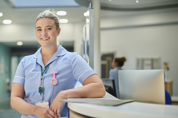 A member of nursing staff standing at a desk and smiling