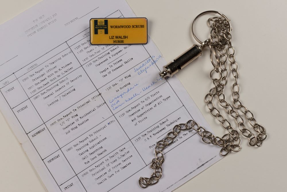 A badge with 'Wormwood Scrubs' and 'Liz Walsh, nurse'. A silver metal whistle on a silver chain. Induction timetable for work.