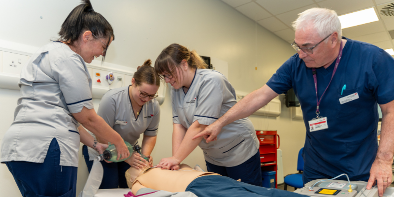 three students working with a dummy while an instructor gives direction