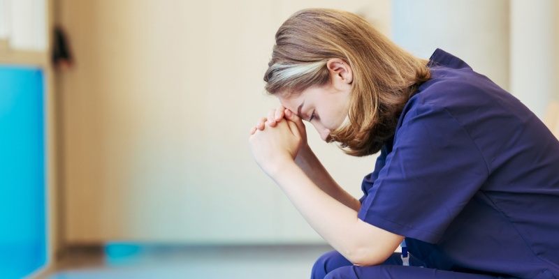 Woman in scrubs with head in hands