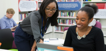 Image of two people in a library looking at a laptop screen