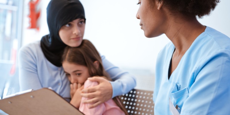 health professional with woman wearing headscarf and scared child