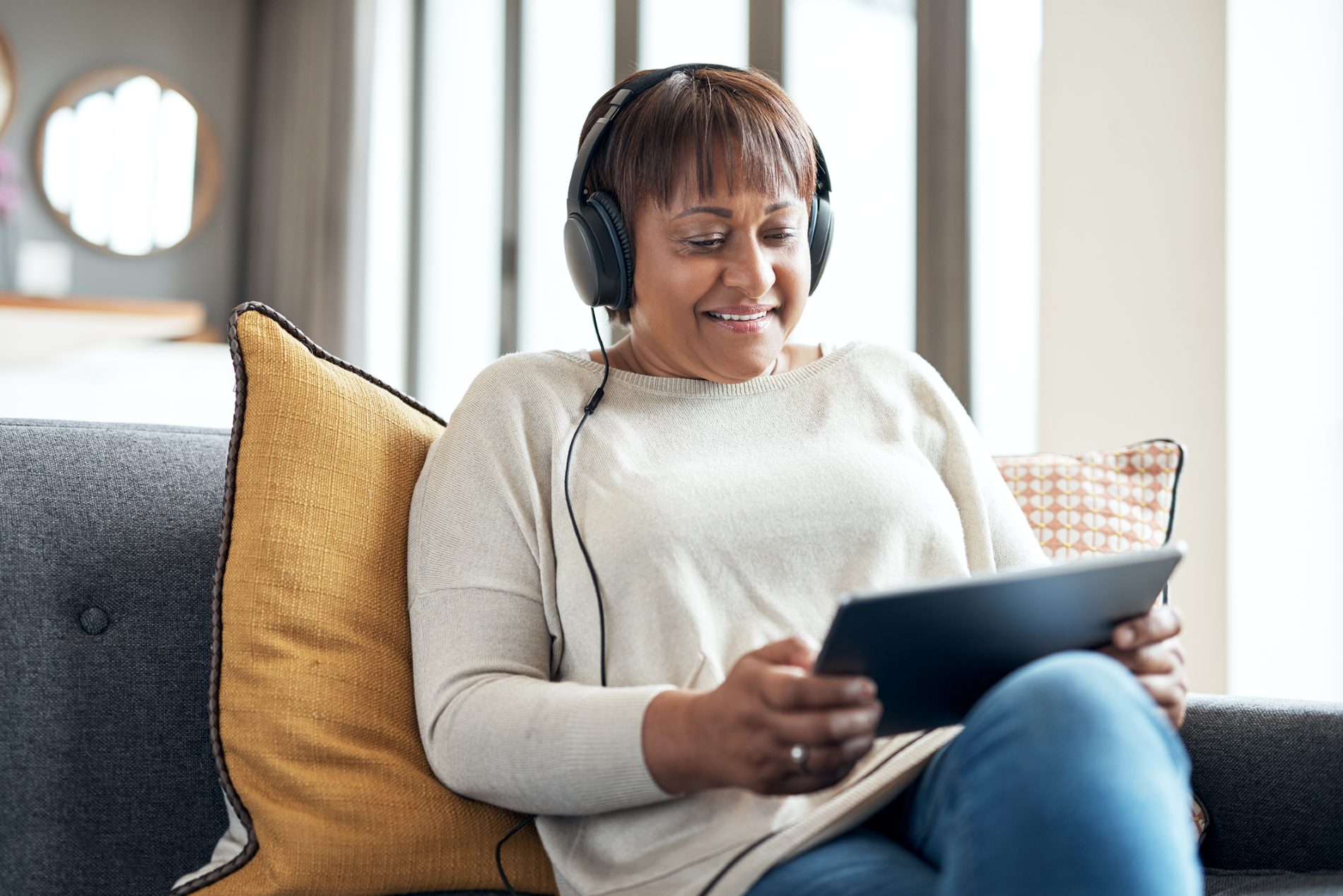 Woman sits on her sofa with tablet and headphones