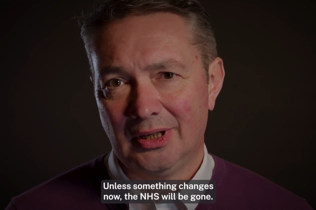 Screen shot of video shows face of male nurse against dark background