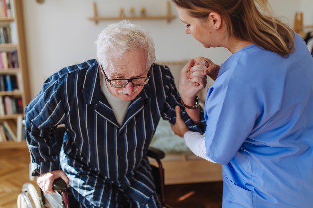 Member of nursing staff helping an older man get up from a chair