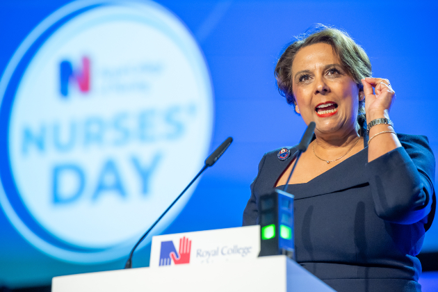 RCN Chief Executive and General Secretary Professor Nicola Ranger is pictured on stage in Liverpool giving her keynote speech. She wears a dark blue dress and stands at a podium, gesturing with a determined look on her face.