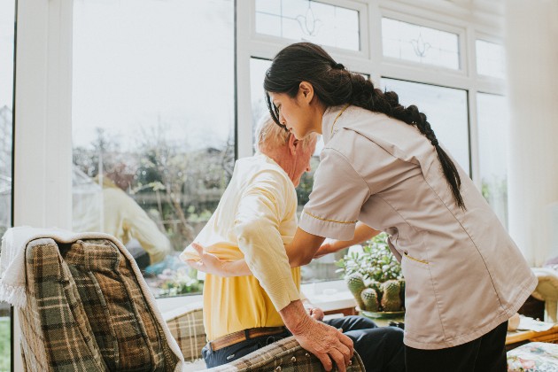 Member of nursing staff helping an older person from their chair