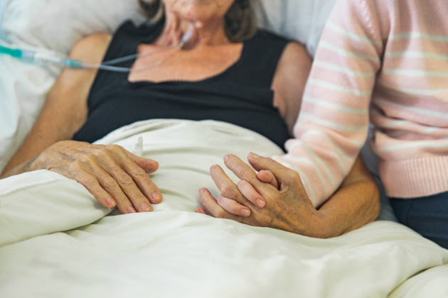 Patient laying in hospital bed holding hands with a visitor