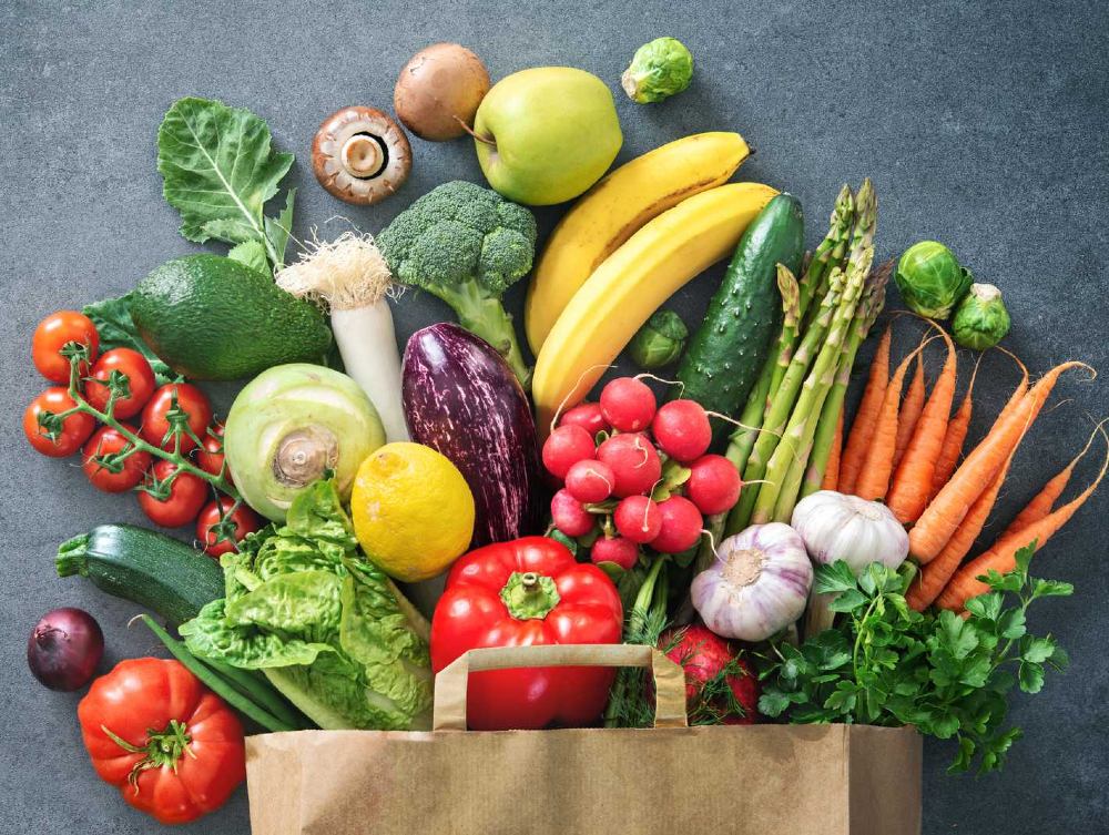 Fruit and vegetables spill out of a brown paper bag