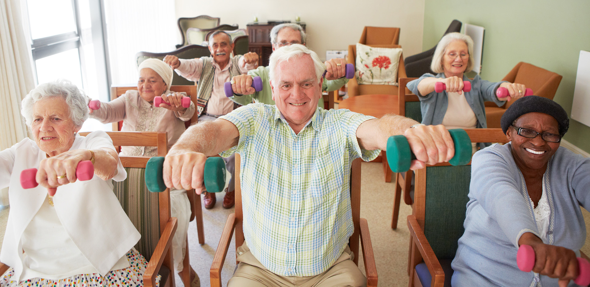 A group of older people do a seated exercise routine using weights