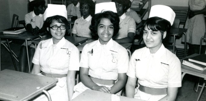 Three BAME nursing students sit together at desks in a classroom